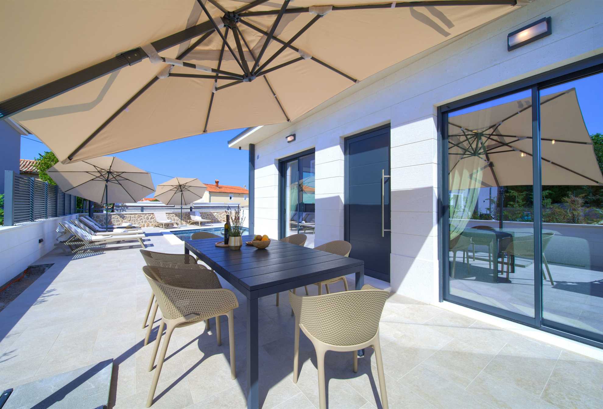 Terrace with chairs and a table in Villa Quarnaro. In the background, there is a pool with sun loungers