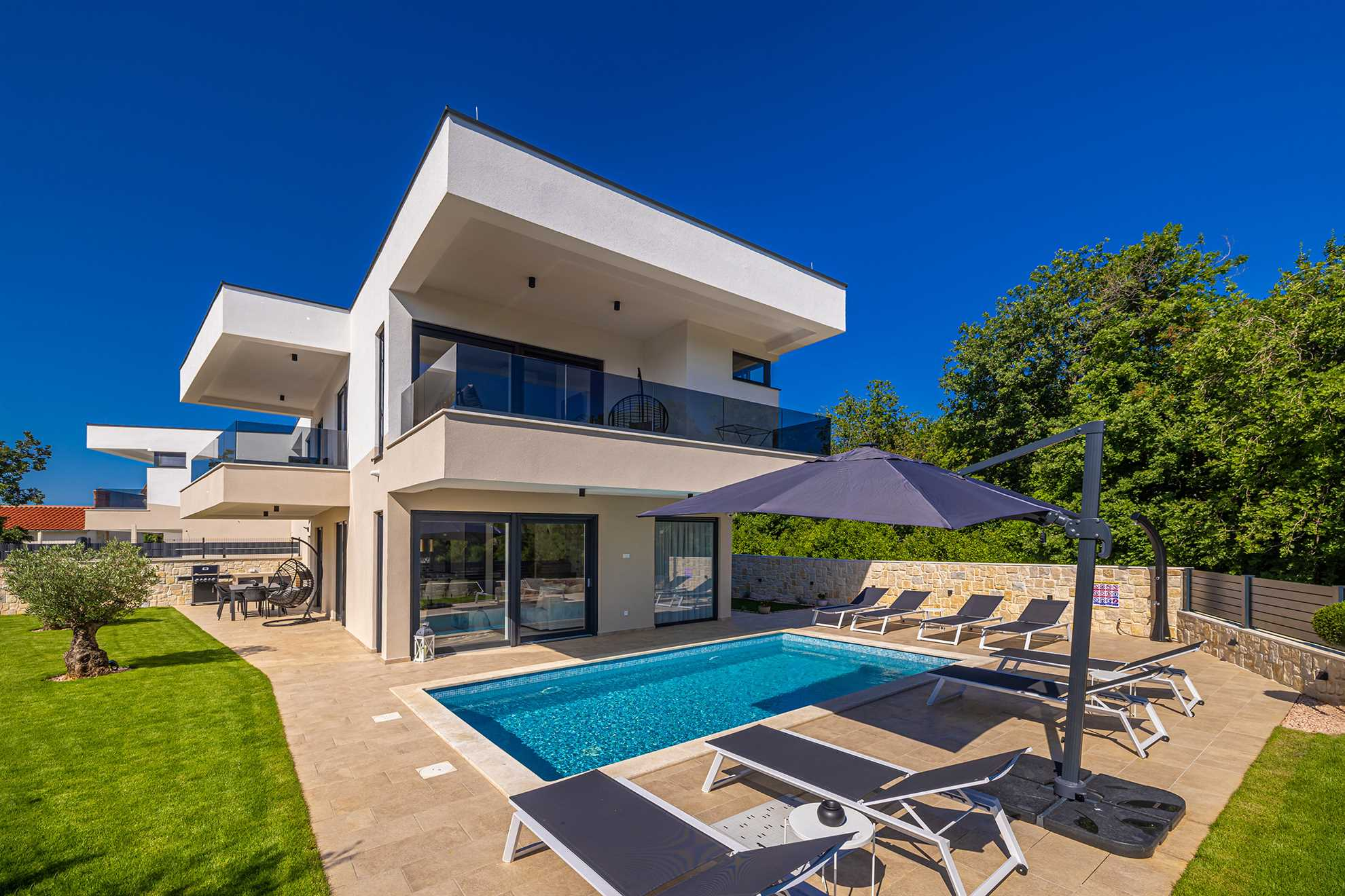 Modernes Ferienhaus OLIVE BLUE in Omišalj mit Pool, Sonnenliegen, Sonnenschirm und großem Garten mit viel Grün.