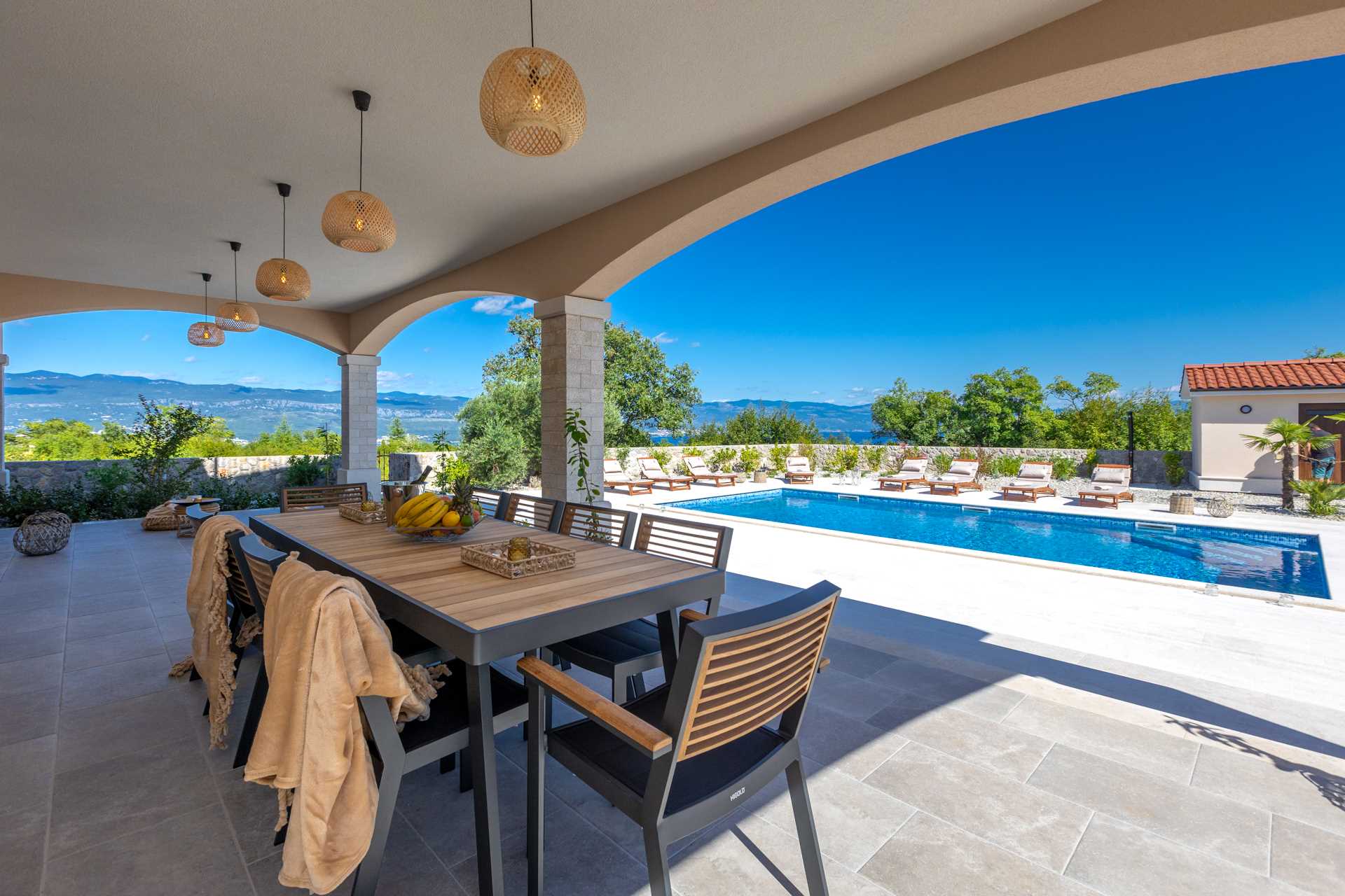 Terrace with dining table overlooking the pool, sun loungers and nature in the background.