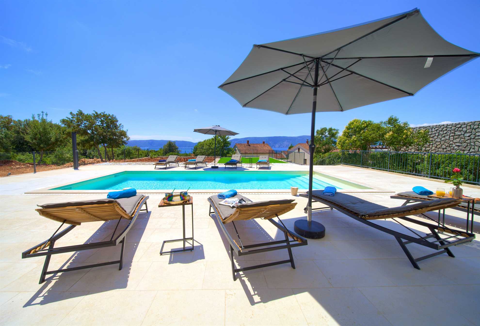 Swimming pool with sun loungers and umbrella for shade.