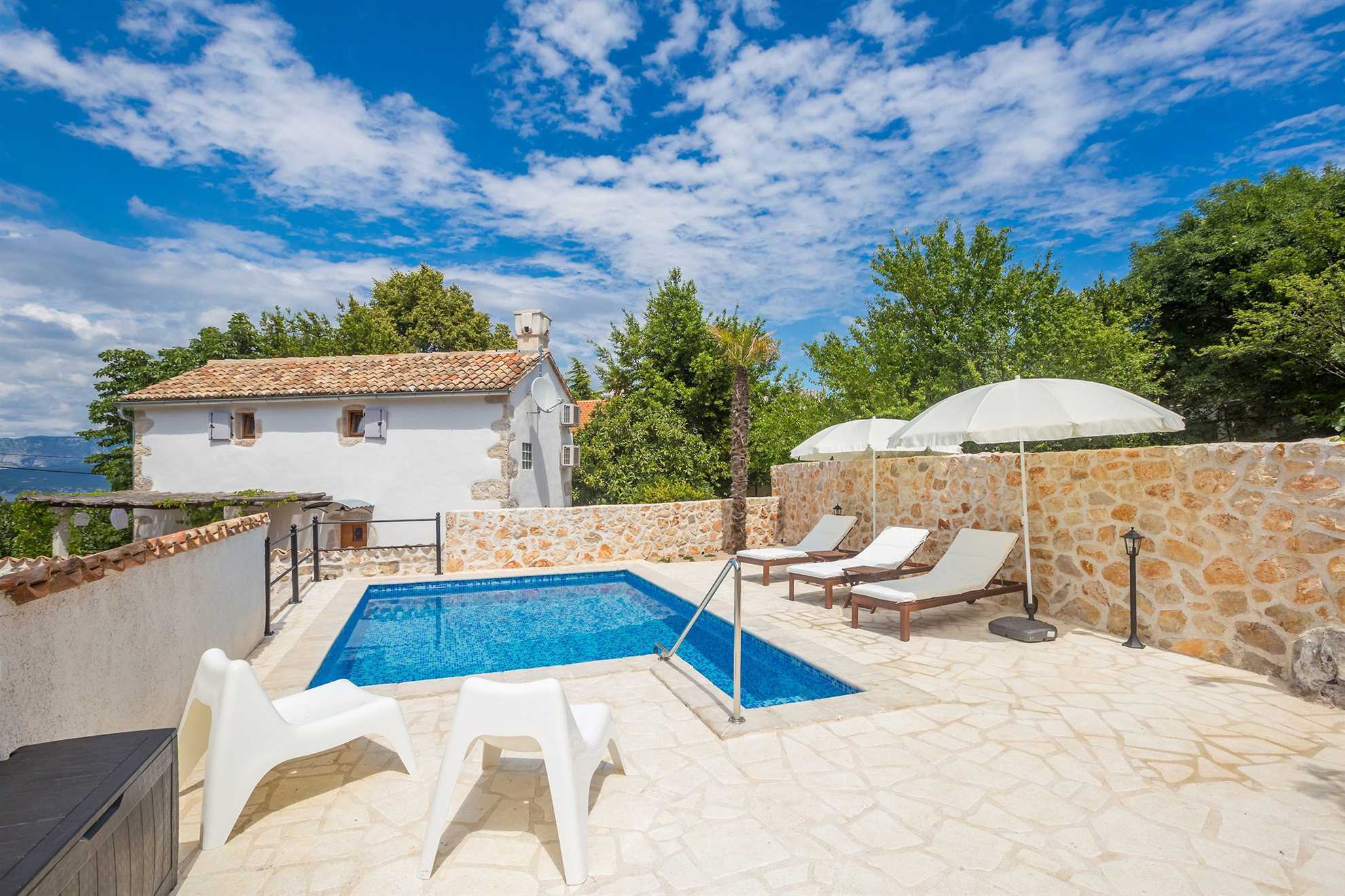 Vacation home with a swimming pool and sun loungers with umbrellas.