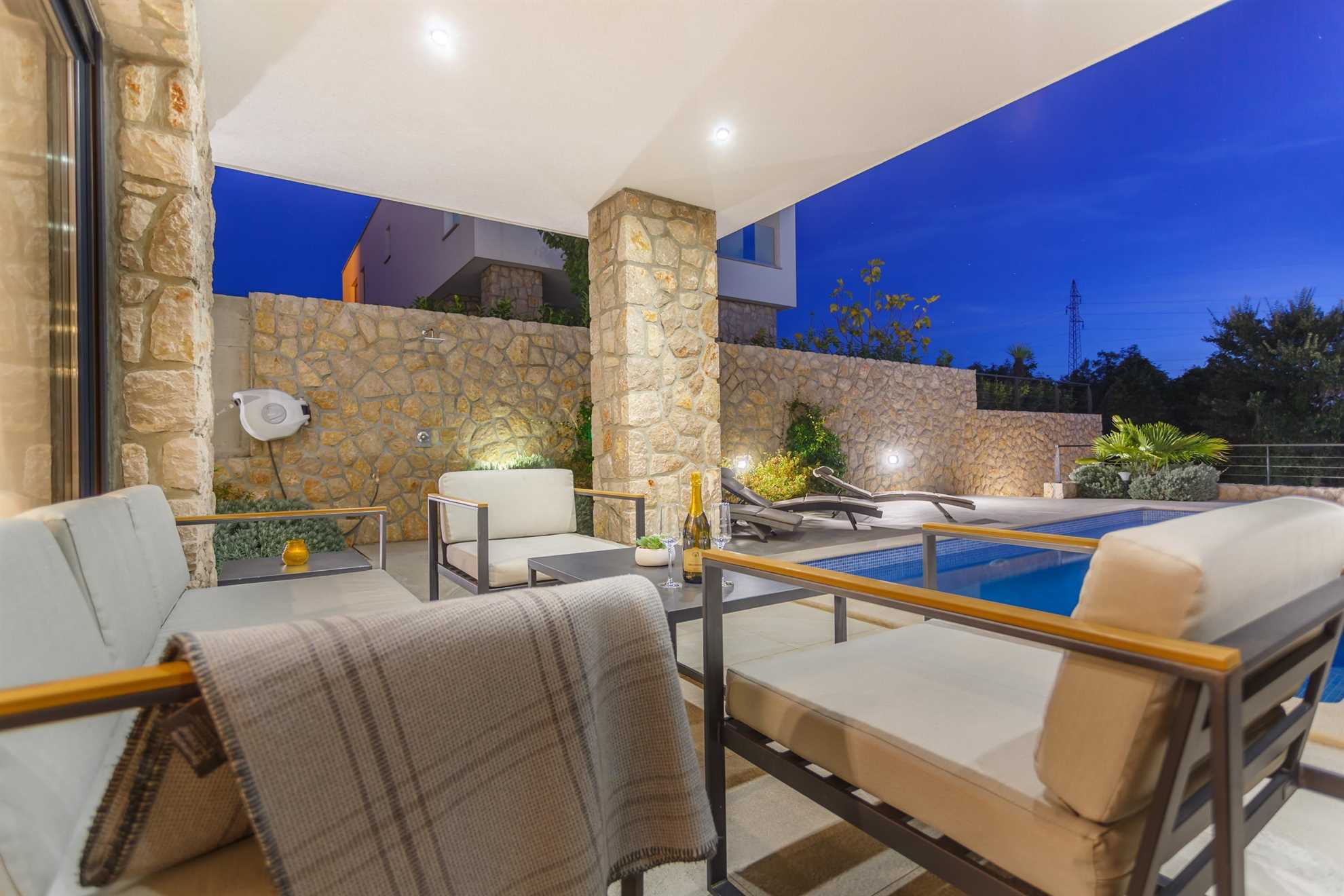 Modern exterior with a small table and modern armchairs next to a pool with sun loungers.