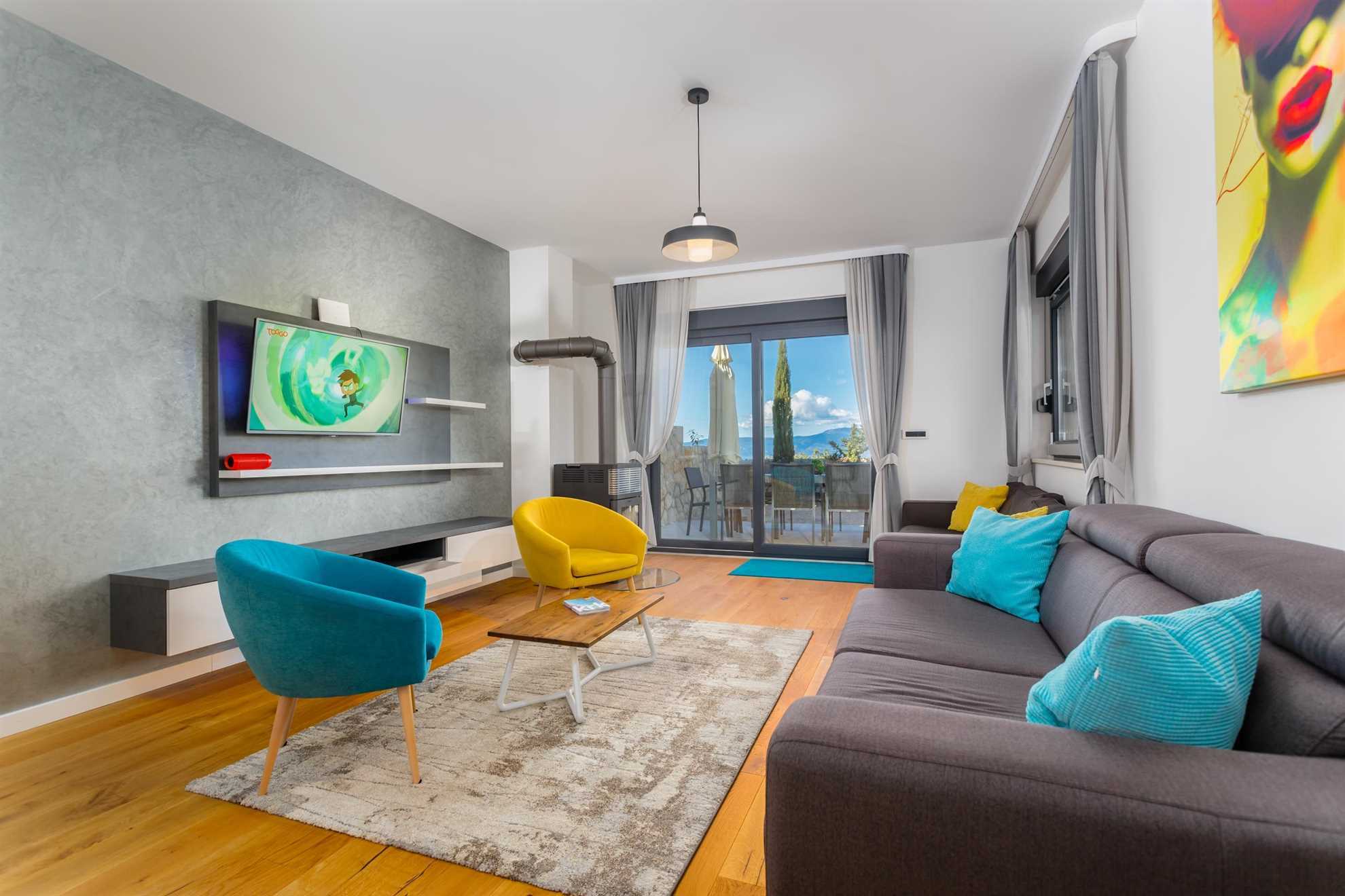 Modern living room with a dark sofa, colorful armchairs, TV and access to the terrace.