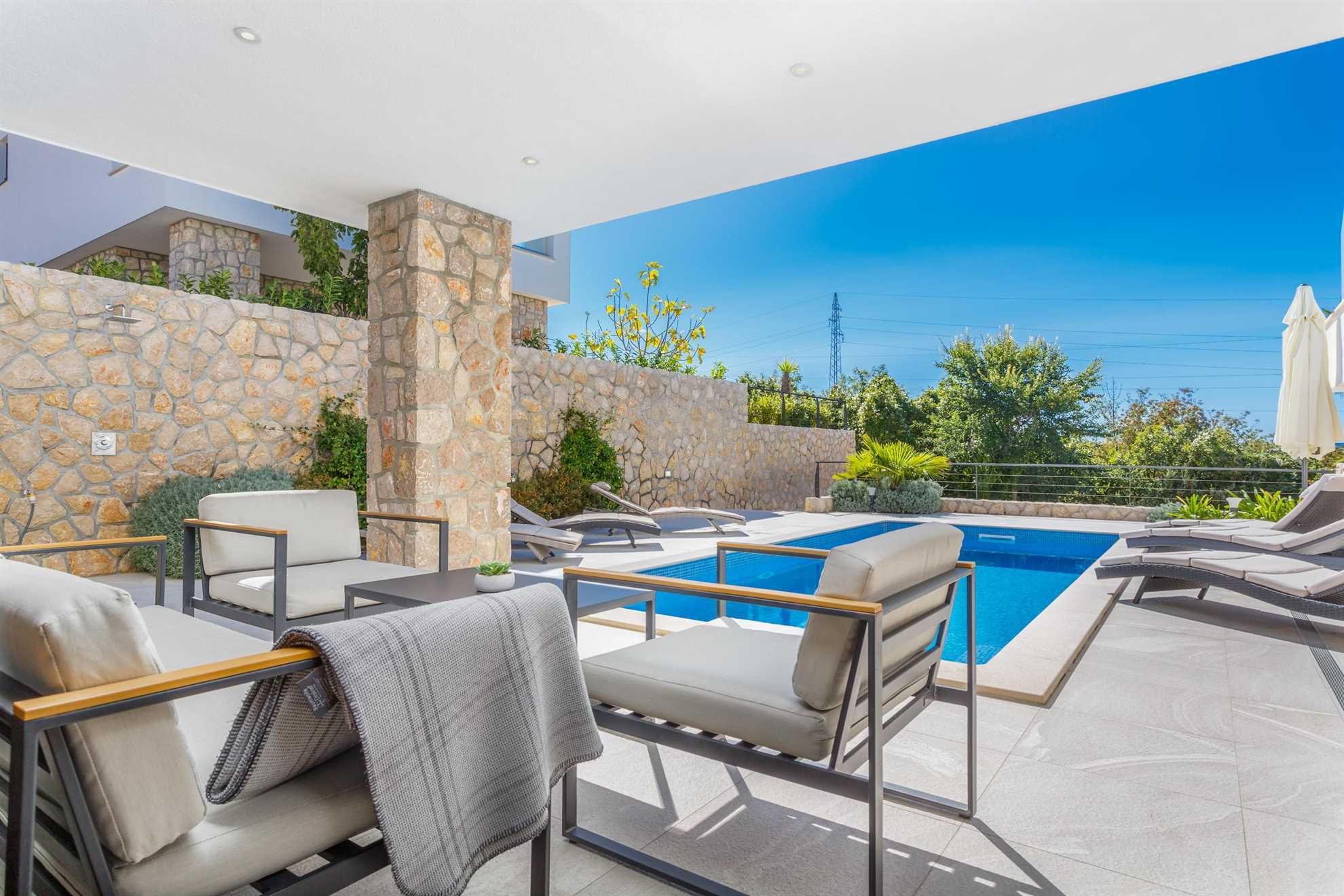 Swimming pool with sun loungers, next to which is a small table with armchairs.