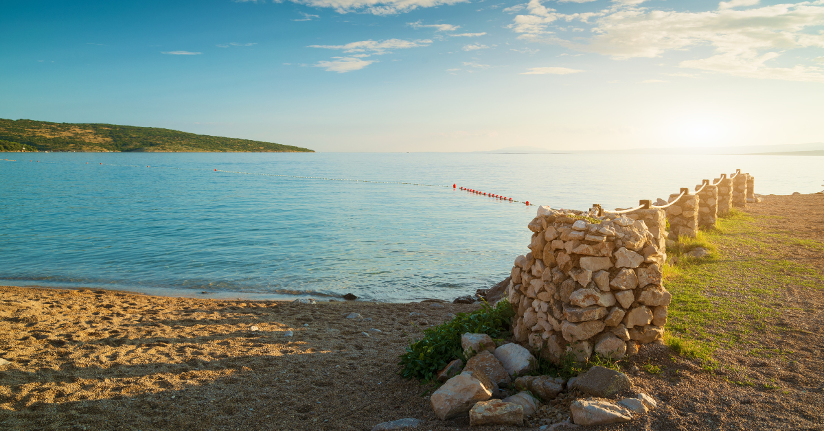 Kameni zid uz pješčanu plažu i more.