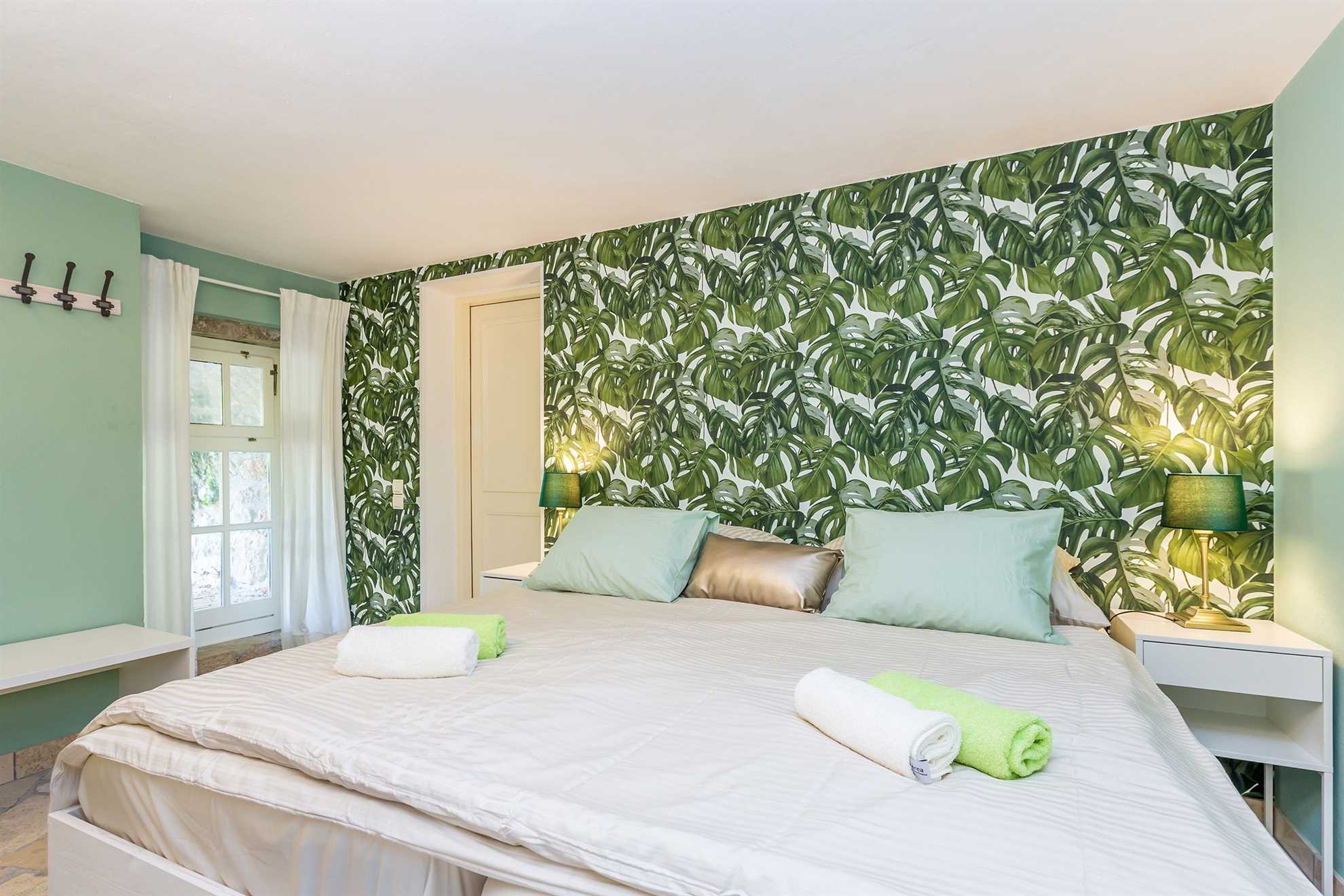 Bedroom with green leaf-shaped wallpapers and a large bed adorned with pillows and towels.