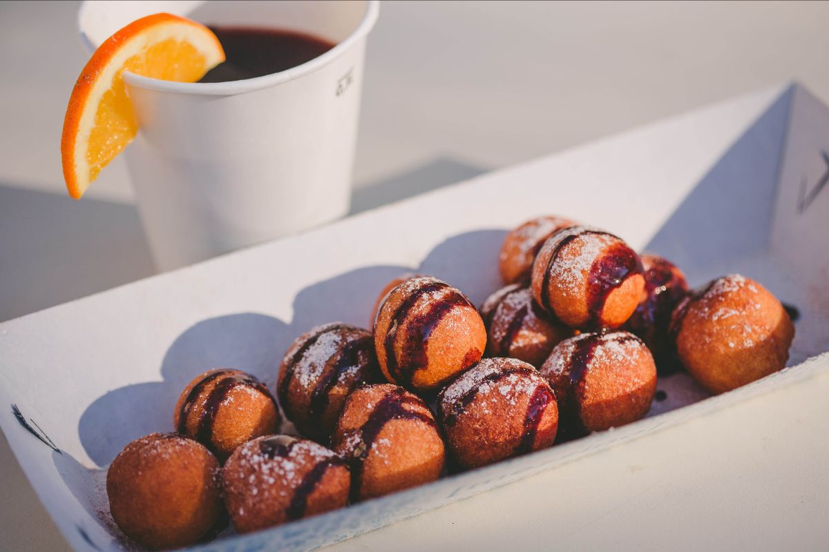 Fritters in a bowl and a black drink with a slice of orange