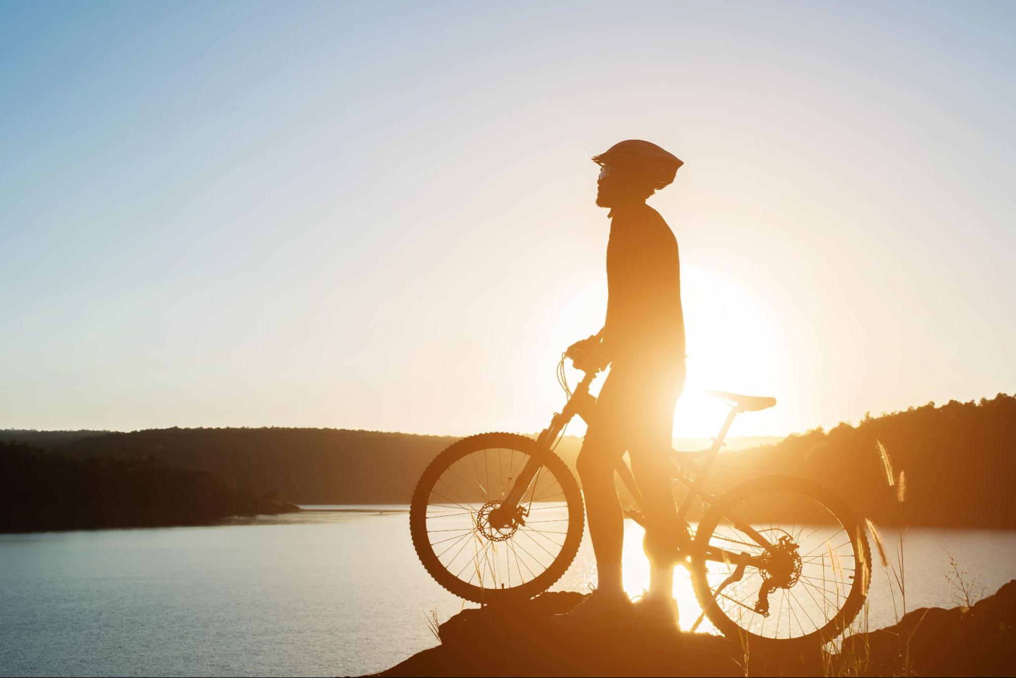 A cyclist with a bicycle on a cliff overlooking the sea.