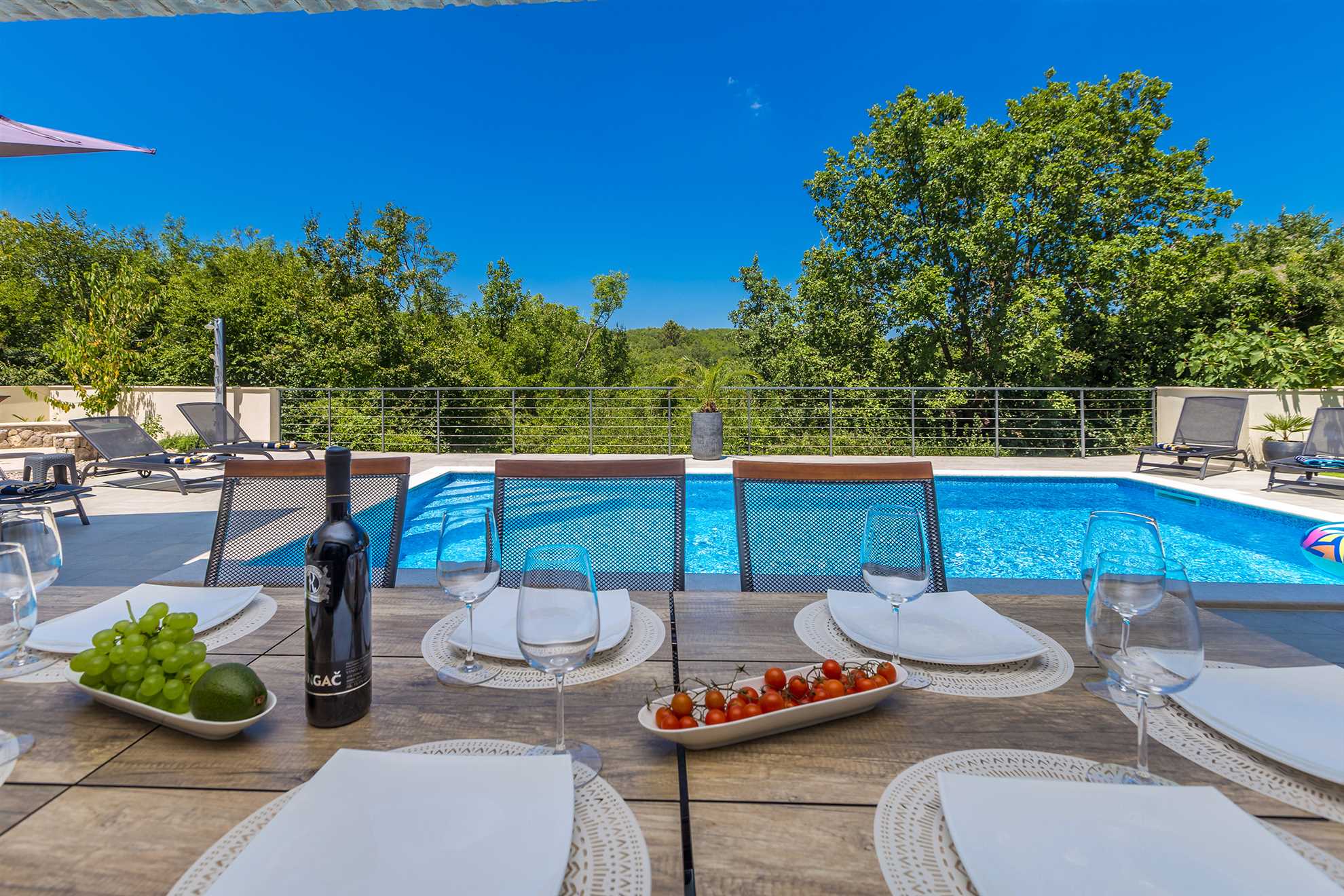 Table with plates and wine glasses next to a swimming pool.